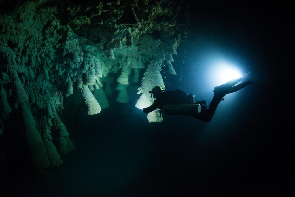Scuba diver exploring unique natural formations known as "bells" in submerged caves beneath the